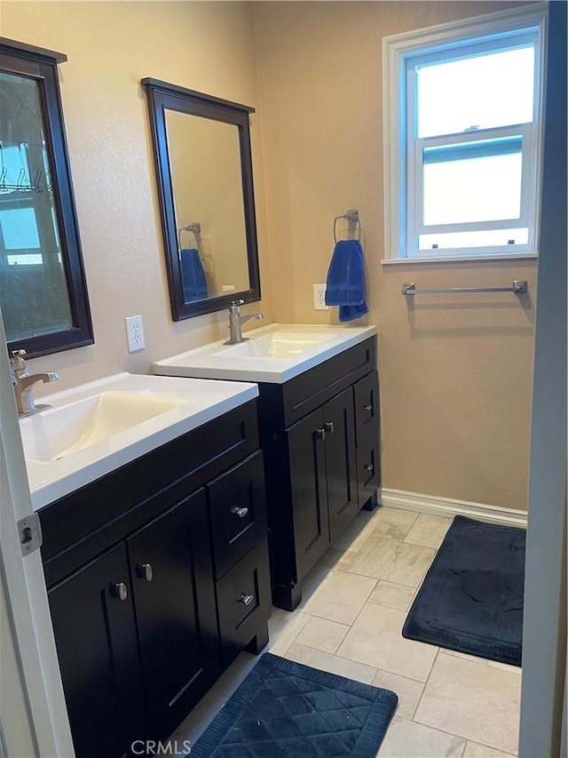 bathroom featuring baseboards, two vanities, and a sink