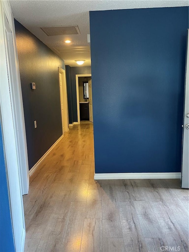 hall featuring baseboards, visible vents, a textured ceiling, and light wood finished floors