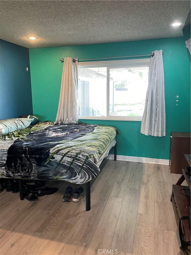 bedroom featuring a textured ceiling, light wood finished floors, and baseboards