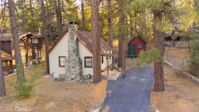 rustic home featuring a chimney, fence, aphalt driveway, and an outdoor structure