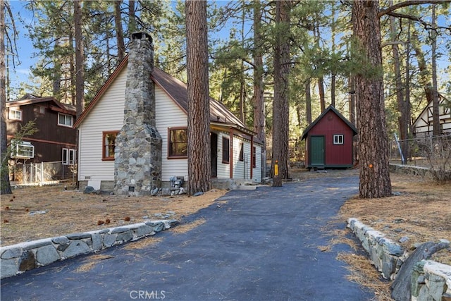 view of property exterior with driveway, a shed, a chimney, and an outdoor structure