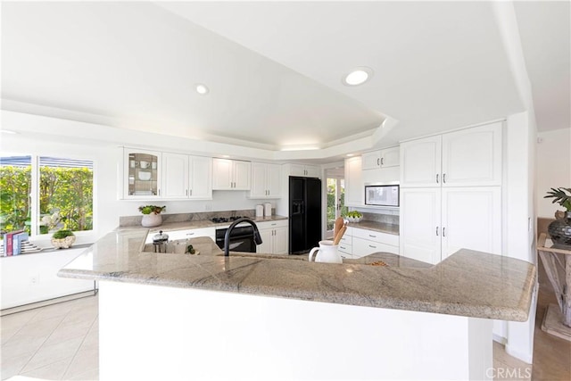 kitchen featuring white microwave, glass insert cabinets, white cabinetry, a peninsula, and black fridge