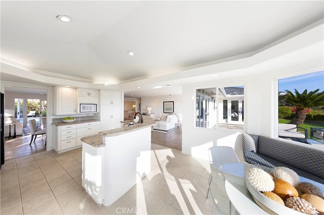 kitchen featuring white microwave, a peninsula, white cabinets, open floor plan, and a raised ceiling