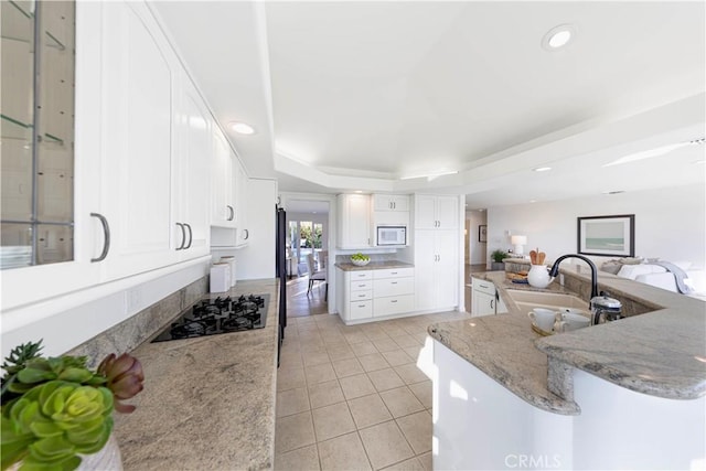 kitchen with a raised ceiling, a peninsula, black gas cooktop, white cabinetry, and a sink