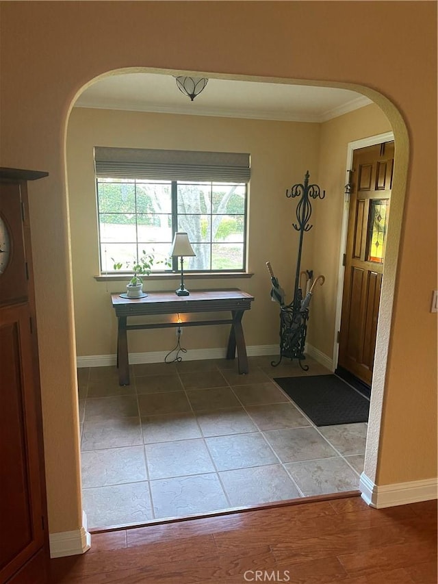 entryway with arched walkways, crown molding, and baseboards