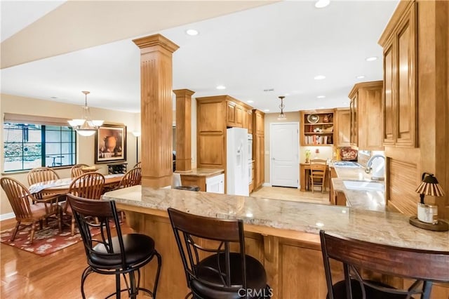 kitchen with a peninsula, white refrigerator with ice dispenser, light wood-type flooring, open shelves, and ornate columns