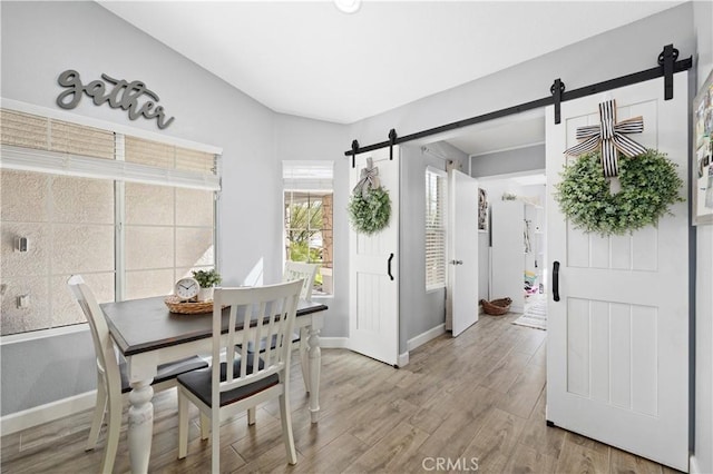 dining area featuring light wood-style floors, a barn door, and baseboards