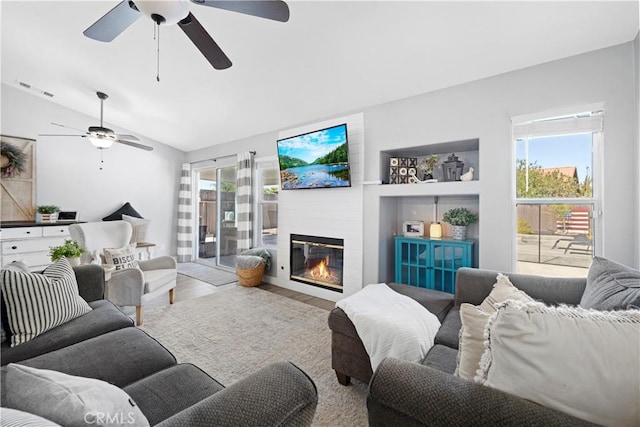 living area with vaulted ceiling, a large fireplace, wood finished floors, and visible vents