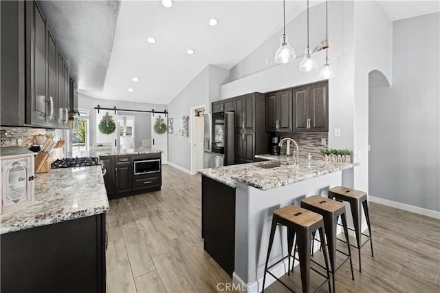 kitchen with a barn door, arched walkways, stainless steel fridge with ice dispenser, a peninsula, and built in microwave