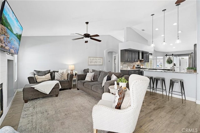 living room featuring ceiling fan, arched walkways, a fireplace, wood finished floors, and baseboards