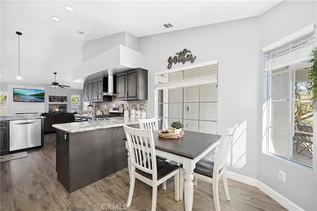 kitchen with a healthy amount of sunlight, wall chimney exhaust hood, stainless steel appliances, and dark wood-type flooring