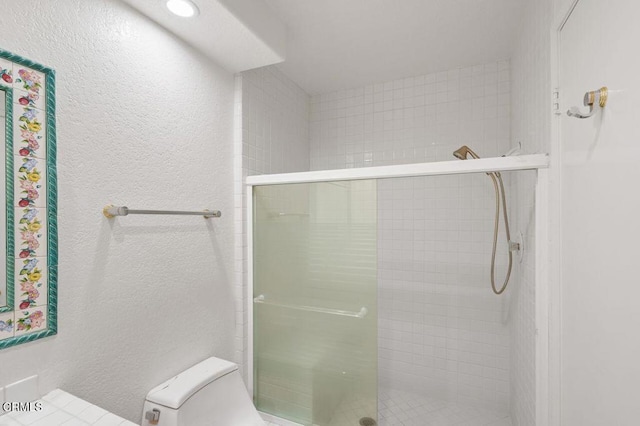 bathroom with a textured wall, a stall shower, and toilet