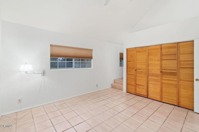 unfurnished bedroom with vaulted ceiling, light tile patterned floors, a closet, and baseboards