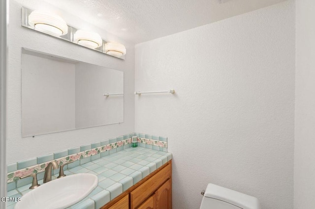 half bath with toilet, a textured wall, a textured ceiling, and vanity