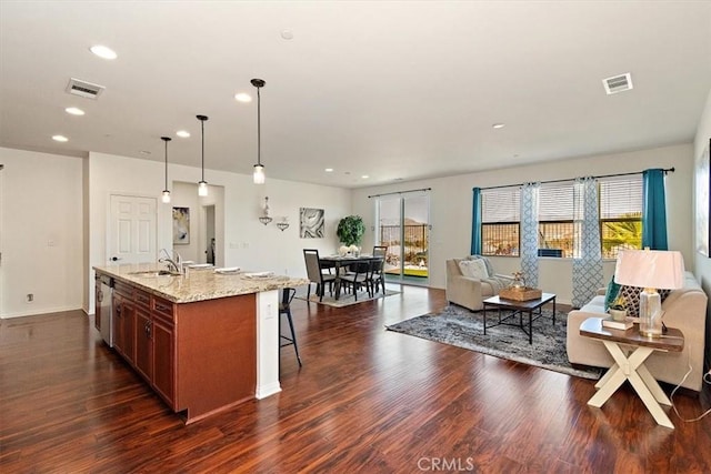 kitchen featuring visible vents, open floor plan, light stone countertops, an island with sink, and decorative light fixtures