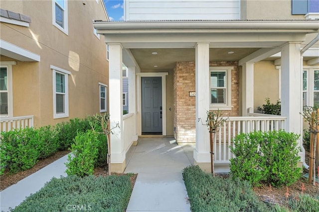 doorway to property with a porch, brick siding, and stucco siding