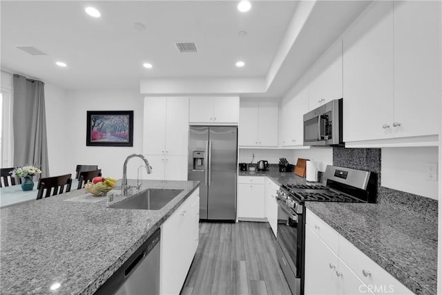 kitchen with light wood finished floors, stainless steel appliances, white cabinets, a sink, and dark stone counters