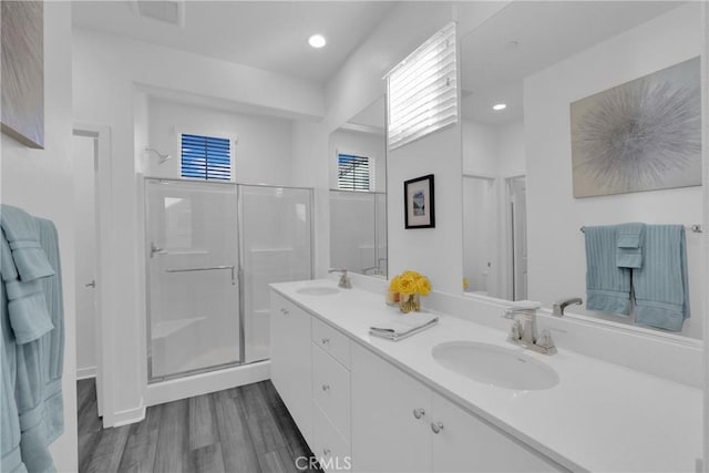 bathroom featuring double vanity, a sink, a shower stall, and wood finished floors