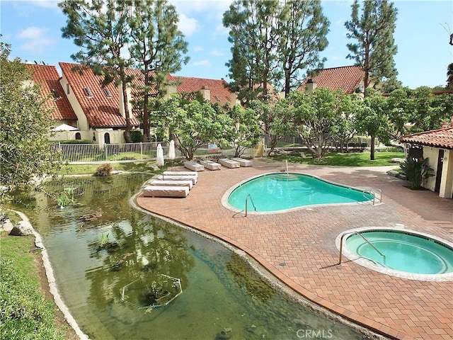 community pool featuring fence and a hot tub