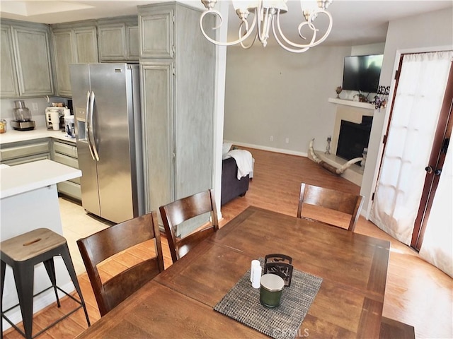 dining space with baseboards, a fireplace with raised hearth, light wood finished floors, and an inviting chandelier