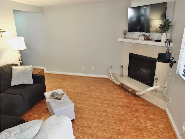 living room featuring baseboards, a fireplace with raised hearth, and light wood finished floors