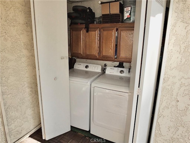 washroom featuring cabinet space, a textured wall, and washing machine and clothes dryer