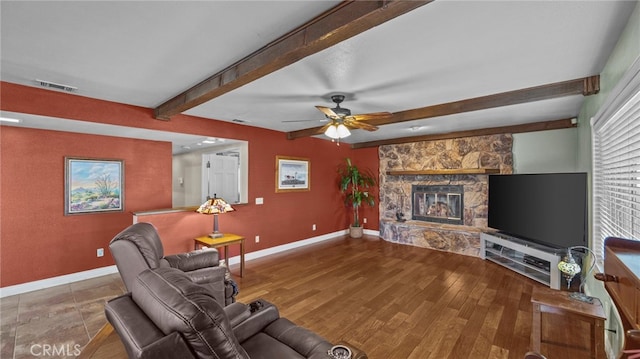 living room featuring baseboards, wood finished floors, beam ceiling, and a stone fireplace