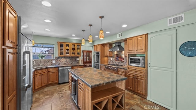 kitchen featuring visible vents, brown cabinetry, wall chimney exhaust hood, butcher block counters, and stainless steel appliances