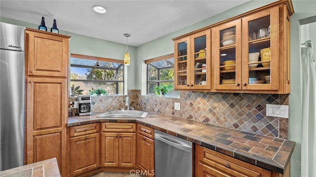 kitchen with tasteful backsplash, tile countertops, appliances with stainless steel finishes, glass insert cabinets, and a sink