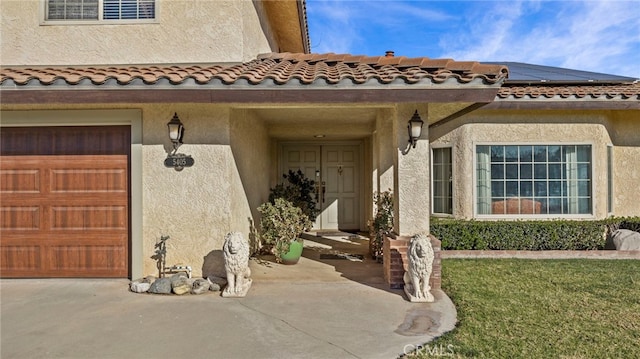 view of exterior entry with a tile roof, visible vents, solar panels, and stucco siding