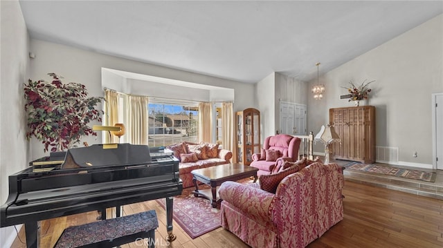 living room featuring visible vents, hardwood / wood-style floors, vaulted ceiling, a chandelier, and baseboards