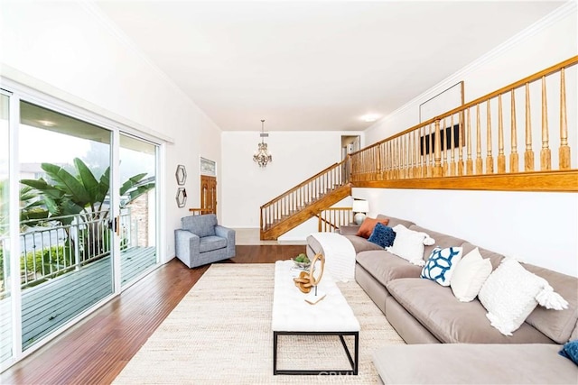 living room featuring dark wood-style floors, a notable chandelier, ornamental molding, and stairs