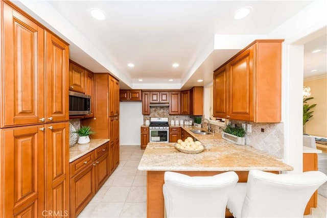 kitchen featuring stainless steel appliances, a breakfast bar, a peninsula, a sink, and light stone countertops