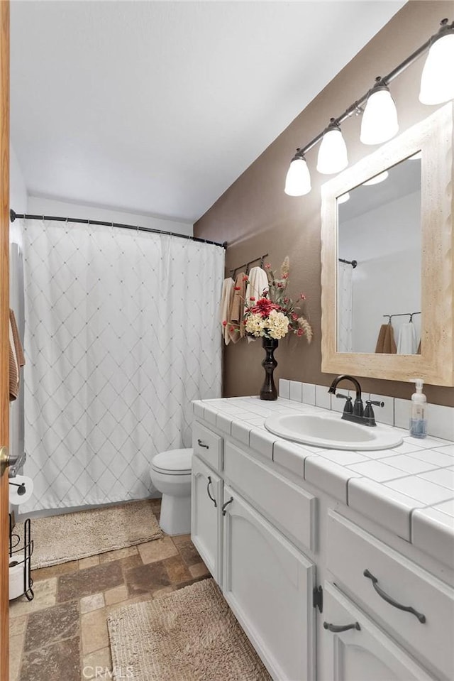 bathroom with toilet, stone finish flooring, and vanity