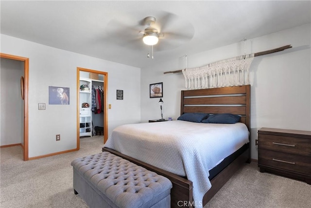 bedroom with light colored carpet, a ceiling fan, baseboards, a closet, and a walk in closet