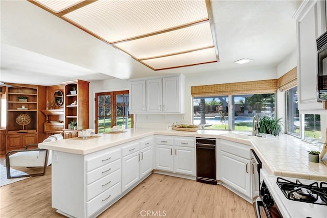 kitchen featuring tile countertops, light wood finished floors, white cabinetry, a sink, and a peninsula