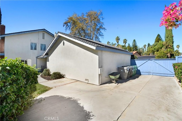 view of property exterior with a gate, a patio area, fence, and stucco siding