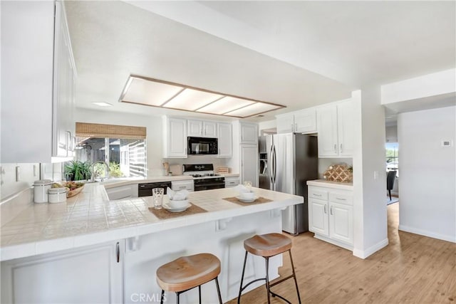 kitchen featuring black appliances, a peninsula, white cabinetry, and a kitchen breakfast bar