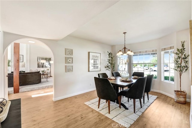 dining area with light wood finished floors, baseboards, arched walkways, and an inviting chandelier