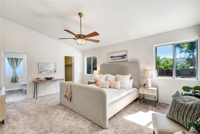 bedroom featuring vaulted ceiling, ensuite bath, a walk in closet, and light colored carpet