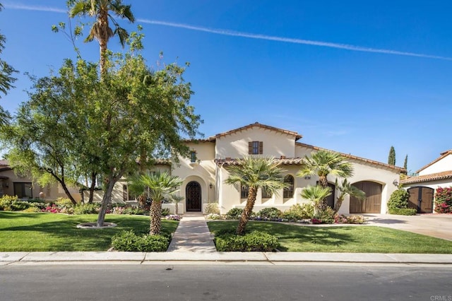 mediterranean / spanish house with a garage, concrete driveway, a front lawn, and stucco siding