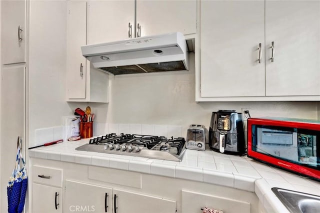 kitchen with stainless steel gas stovetop, white cabinetry, tile counters, and under cabinet range hood