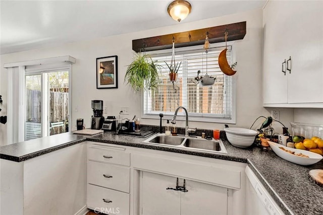 kitchen with dark countertops, white cabinets, a sink, dishwasher, and a peninsula