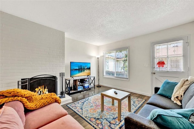 living room featuring a textured ceiling, a brick fireplace, wood finished floors, and baseboards