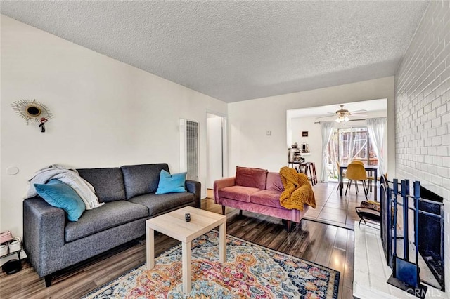 living room featuring a ceiling fan, a fireplace, a textured ceiling, and light wood finished floors