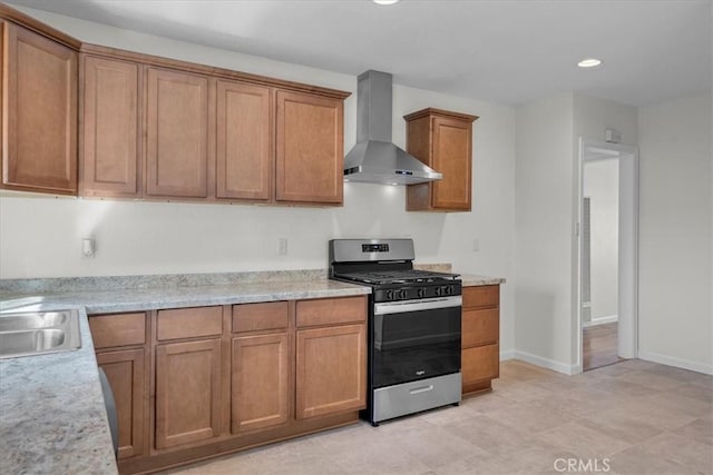 kitchen featuring wall chimney range hood, recessed lighting, stainless steel range with gas cooktop, brown cabinetry, and a sink