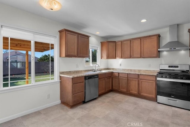 kitchen featuring appliances with stainless steel finishes, brown cabinetry, wall chimney range hood, and baseboards