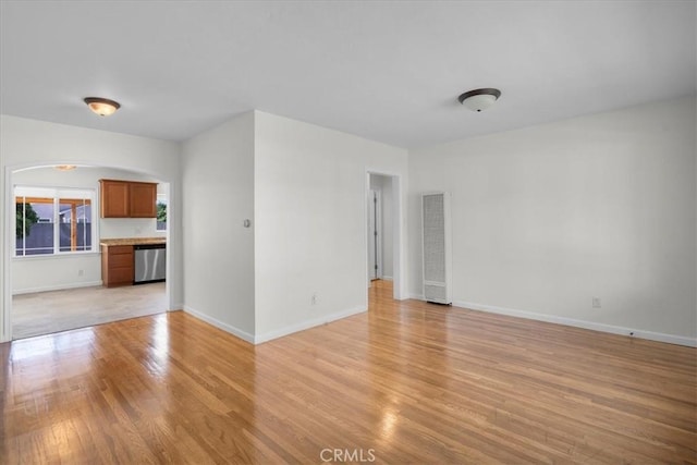 unfurnished living room featuring arched walkways, light wood finished floors, and baseboards