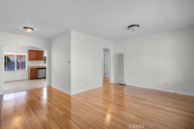 unfurnished living room featuring arched walkways, light wood-style floors, and baseboards