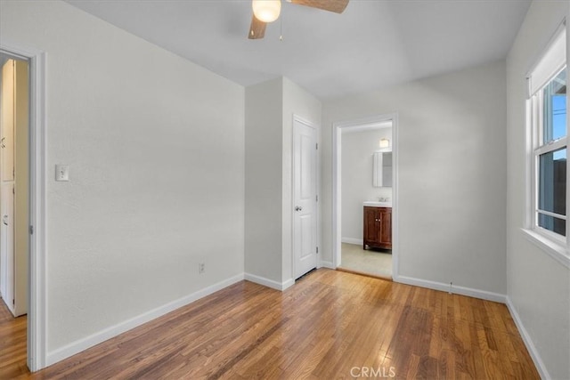 unfurnished bedroom featuring ensuite bath, light wood-type flooring, baseboards, and ceiling fan